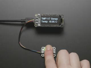 Finger on sensor connected to a Feather via QT cable, with OLED wing showing skin temperature