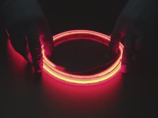 Two hands repeatedly bending and manipulating lit-up flexible red LED strip