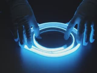 Two hands repeatedly bending and manipulating lit-up flexible blue LED strip