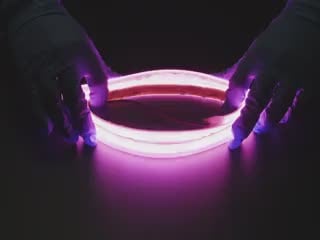 Two hands repeatedly bending and manipulating lit-up flexible pink LED strip