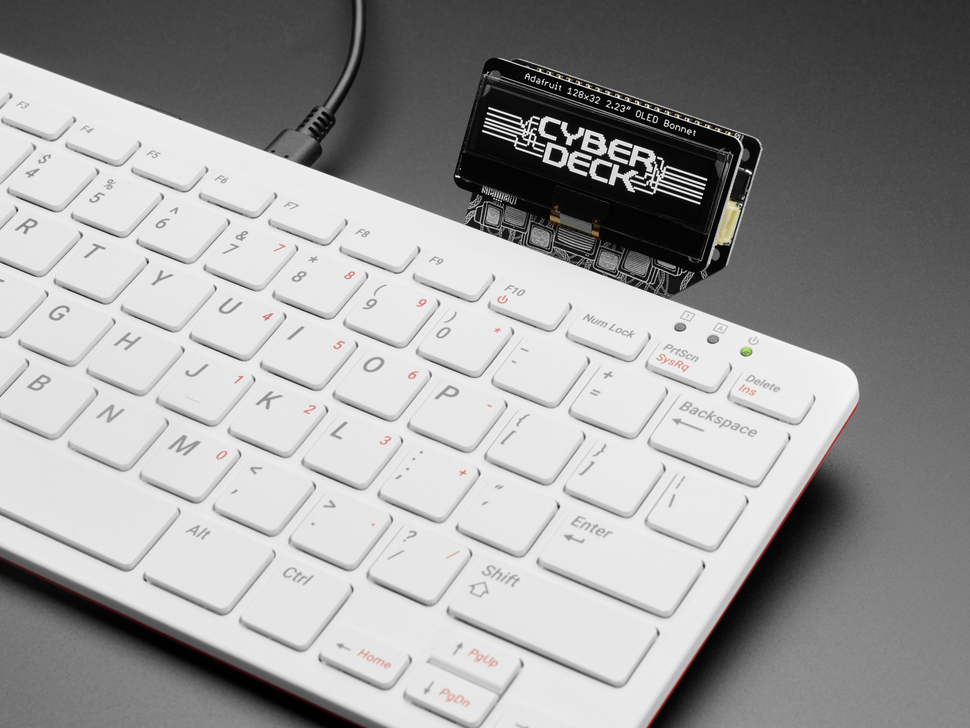 Angled close-up of black and white OLED display assembled onto Pi 400 keyboard computer. The display reads: CYBDERDECK in a cyberpunk font.