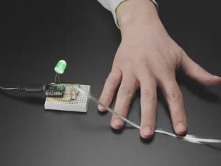 Video of a hand scrunching the ribbon sensor triggering a green LED installed on a breadboard to light up.