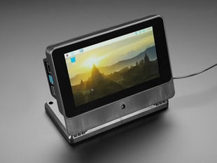 Angled shot of assembled SmartPi Touch Pro. The touchscreen displays a wallpaper of a European cityscape at sunrise.