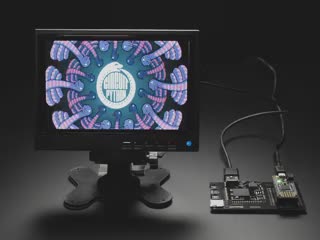 A small monitor and a Gameduino Dazzler PCB with a Feather M4 Express. The monitor displays a swirling kaleidoscopic animation with CircuitPython and Blinka, a friendly coding python.