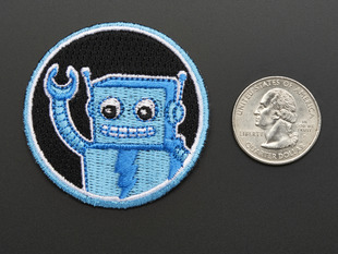 Circular embroidered badge with friendly blue robot waving on black background with blue trim, next to quarter for scale. 