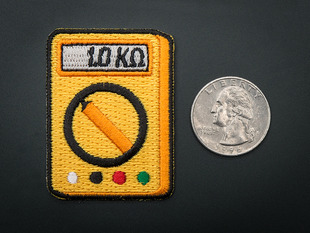 Rectangular embroidered badge in the shape of orange multimeter with dial, and a grey screen reading 1.0 kilohms. Next to quarter for scale 