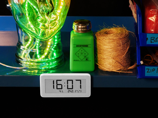 Shot of a work station shelf populated with electronic tools and a clear glass head filled with glowing LED strips. The eInk clock sits below reading the time, temperature, and humidity.