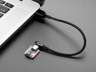 Angled shot of a black woven USB cable plugged into a laptop port and a small dev board.