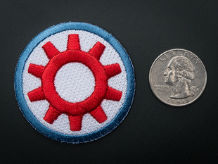 Circular embroidered badge with red gear on white background and blue trim. Next to quarter for scale. 