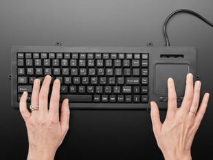 Top view of a white woman's hands typing on full-size keyboard with trackpad.