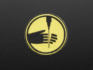 Circular embroidered badge showing left hand with fingers severed by water pick, in black on yellow background, with black edge.  