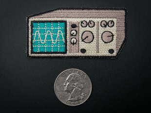Embroidered badge of analog oscilloscope in grey with turquoise screen showing sine wave, next to a quarter with scale. 