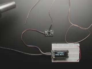 Top view video of an OLED FeatherWing plugged into a Feather M4 board which is connected to the MCP9001 breakout via STEMMA QT cable. A hot air nozzle hovers over the thermocouple, and the OLED displays the rising temperature sensor data.