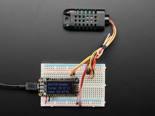 Top view of black humidity sensor sensor wired to a breadboard with an FeatherWing OLED display. The OLED shows the data from the temperature-humidity sensor.