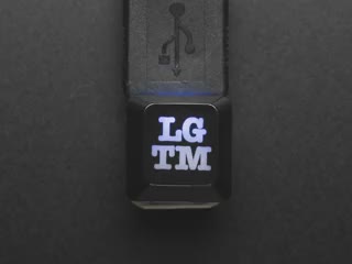 Top view video of black LGTM keycap connected via USB cable. Various colors emit through the logo.
