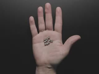 Video of a white hand holding ten wireless LED inductors in the palm of their hand. A small inductive coil is placed over the LEDs which light up red.