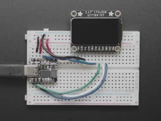 TFT display breakout soldered and assembled onto a half-size breadboard and wired up to a microcontroller. The color TFT screen displays a boot-up screen.