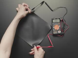 Video of a pressure-sensitive conductive sheet pulled by the corners, which are clipped to alligator test leads and a multimeter. The multimeter displays the fluctuations in resistance.