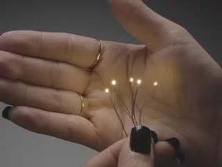 Video of a five mini wired LEDs emitting warm white light against a white open palm.