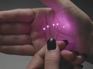 Video of a five mini wired LEDs emitting pink light against a white open palm.
