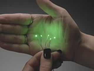 Video of a five mini wired LEDs emitting green light against a white open palm.