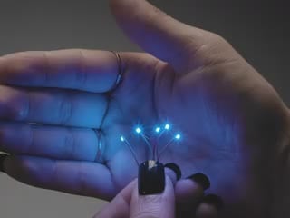 Video of a five mini wired LEDs emitting Blue light against a white open palm.