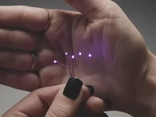 Video of a five mini wired LEDs emitting Purple light against a white open palm.