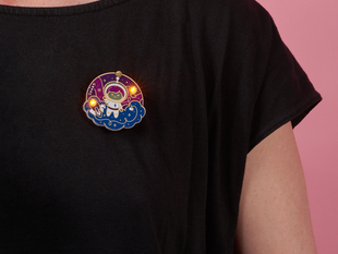 Close crop of PCB badge of a cartoon space girl on a black t-shirt worn by a white person.