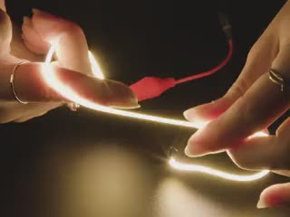 Close-up video of pair of white hands coiling and playing with a 300mm long warm white LED filament.