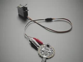 Video of a servo connected via shrouded servo cable with male jumper wires to a circular microcontroller. The servo rotates.