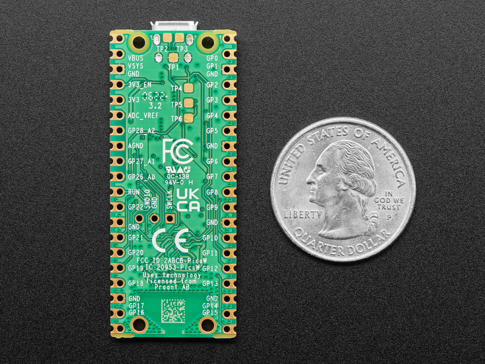 Bottom of a green microcontroller with castellated pads lain vertically next to a US quarter for scale.
