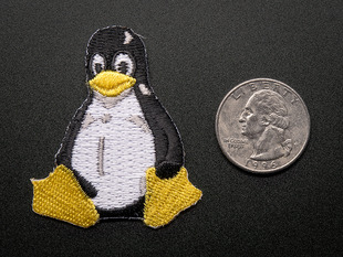 Embroidered badge in the shape of the sitting penguin Linux logo. In black and white, with yellow beak and feet. Shown next to a quarter for scale. 