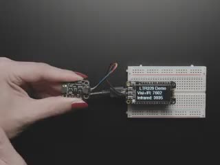 Overhead video of a white person's hand covering a light sensor breakout, which changes the visibility and infrared data on an OLED display breakout.