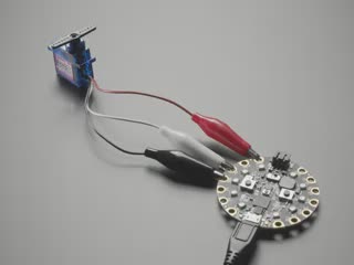 Video of a servo with alligator clips connected to a round microcontroller with pads. The horns on the servo oscillate.