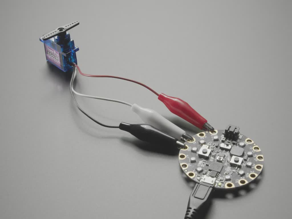 Video of a servo with alligator clips connected to a round microcontroller with pads. The horns on the servo oscillate.
