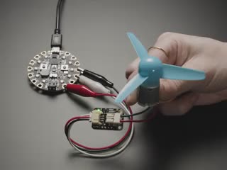 Video of a blue plastic propeller fan installed on a MOSFET motor driver hooked up to a round microcontroller via alligator clips. The blue propeller fan oscillates on and off in short bursts.