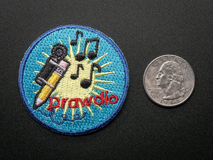 Circular embroidered badge with drawdio machine attached to a pencil, musical notes over a yellow light burst, on a blue background, with the word DRAWDIO in red. Shown next to a quarter for scale. 