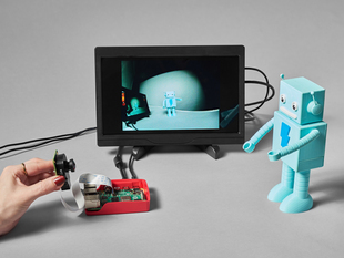 Lifestyle image of a friendly robot figurine used as a Raspberry Pi camera module subject. The lens on the camera is wide angle.