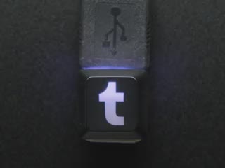 Overhead video of a chonky USB cable adapter with a black keycap. The keycap is etched with the Tumblr logo and glows blue.