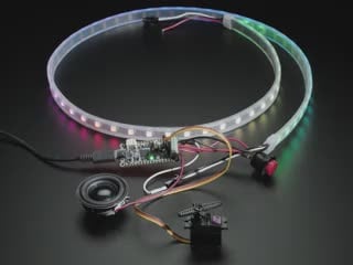 Video of a white hand pressing a button to briefly turn an LED strip into white lights. Also wired up to the microcontroller are a servo motor and a speaker.