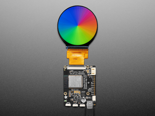 Overhead shot of round TFT display connected to a black, rectangular microcontroller. The TFT displays a rainbow color gradient.