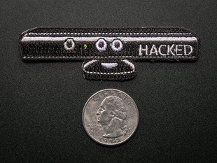Embroidered rectangular badge in the shape of black Kinect box as seen from the side, with the word HACKED in white. Shown next to a quarter for scale. 
