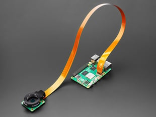 angled shot of green, credit-card-sized microcontroller connected via a 500mm long FPC ribbon cable to a camera module.