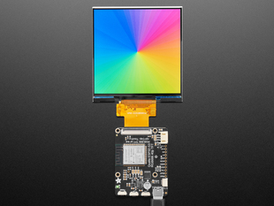 Overhead shot of a 4" square TFT screen connected to a microcontroller. The screen displays a colorful rainbow gradient. A white hand draws a heart on the screen.