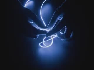 Video of Black hands playing with a 1.2m long LED filament glowing blue light.