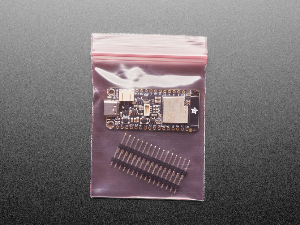 Overhead shot of a rectangular microcontroller with two sticks of 16-pin header in a pink, antistatic bag.