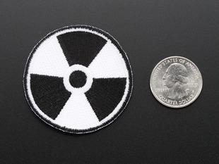 Circular embroidered badge of radiation hazard flag in black and white. Shown next to a quarter for scale. 