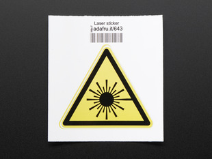 Triangle shaped yellow sticker with laser symbol in black,  trimmed in black. Shown on white paper mount with barcode. 