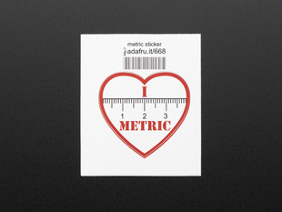Heart shaped sticker with the numbers 1, 2, 3 and the markings of a ruler in black over a white background. The words I and METRIC in red above and below the ruler. The sticker is trimmed in red and mounted on white paper with barcode