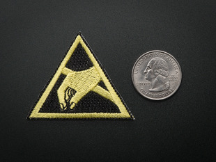 Triangle shaped embroidered badge with yellow hand reaching to pick something up, over a black background, with yellow trim. Shown next to a quarter for scale. 